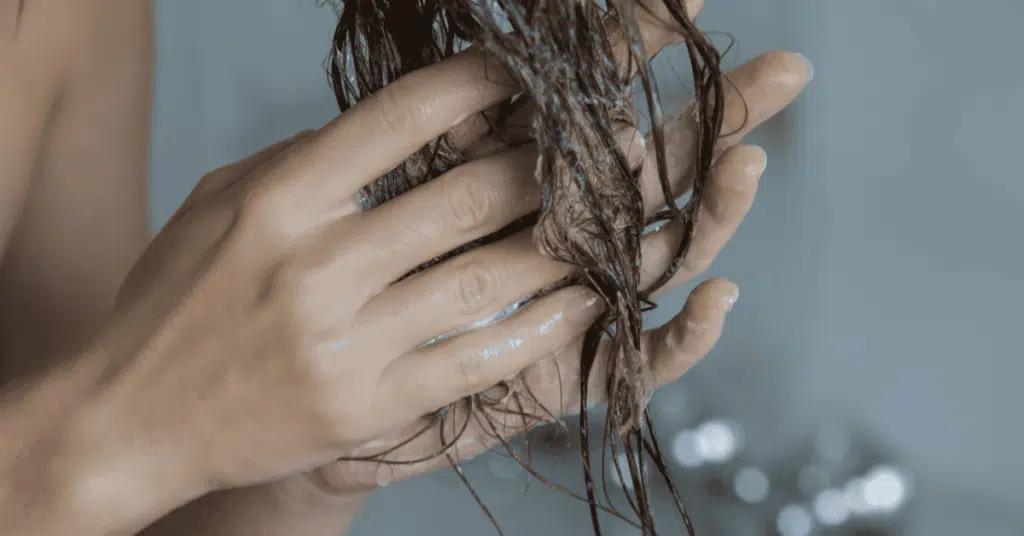 Close-up of woman applying conditioner to the mid-lengths and ends of wet hair