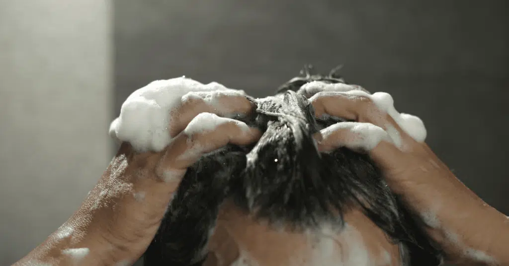 Woman with wavy hair gently shampooing her scalp under lukewarm water